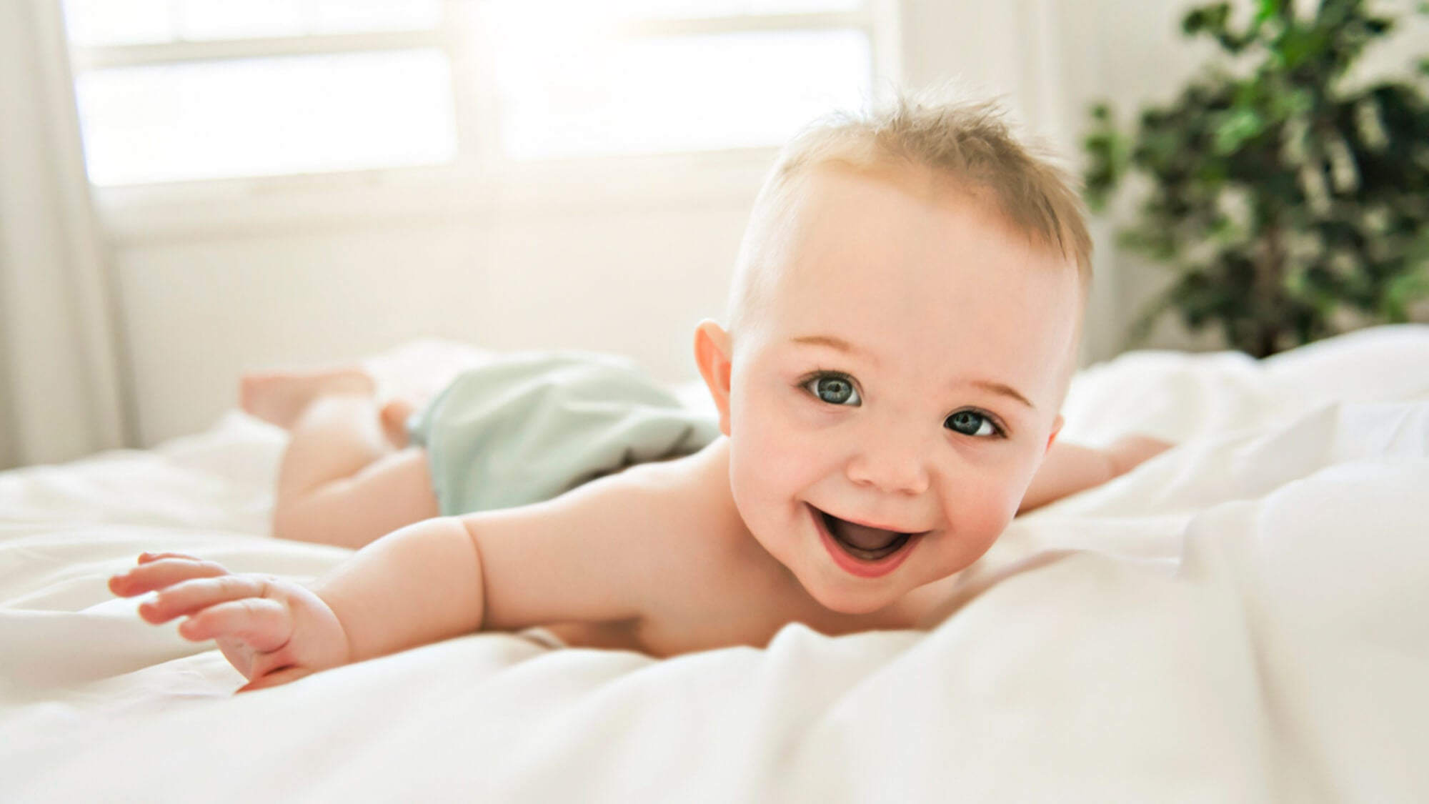 Baby liegt mit einer Stoffwindel auf dem Bett