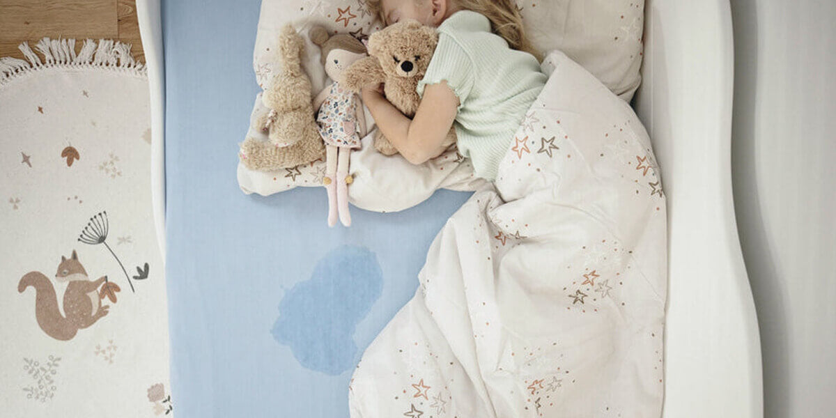 Kleines Kind liegt im Bett mit Urinfleck auf Matratze